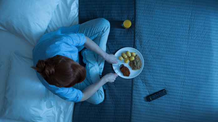 Donna che mangia di notte sul suo letto